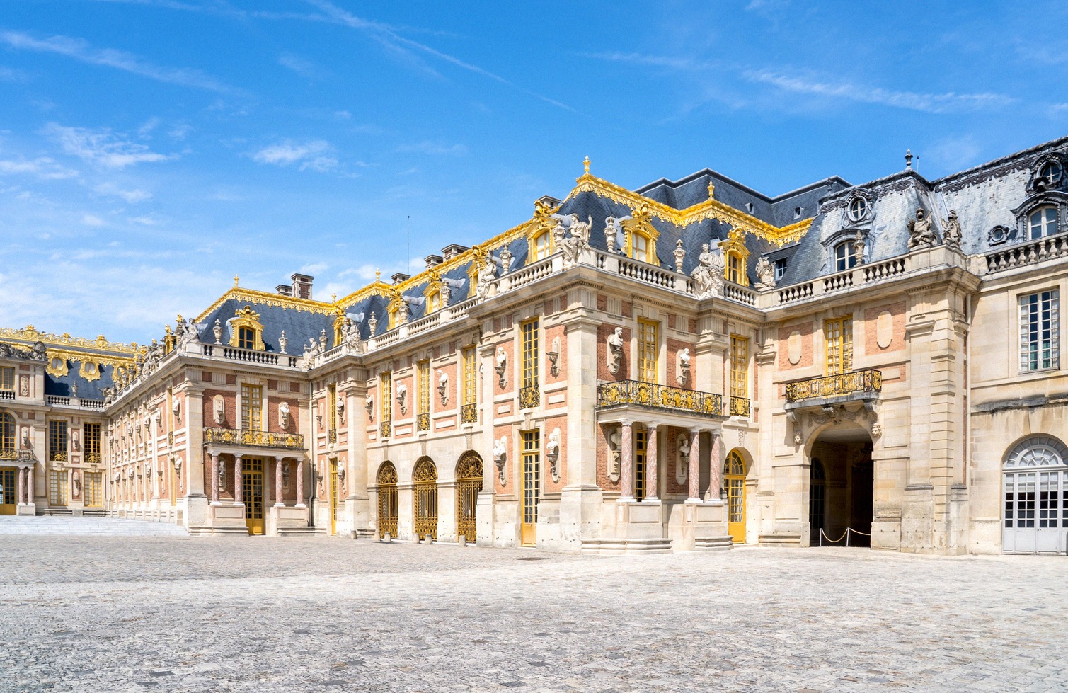 The gilded Baroque facade at the Marble Courtyard (Cour de Marbre) of the Palace of Versailles, with a red-and-white wall