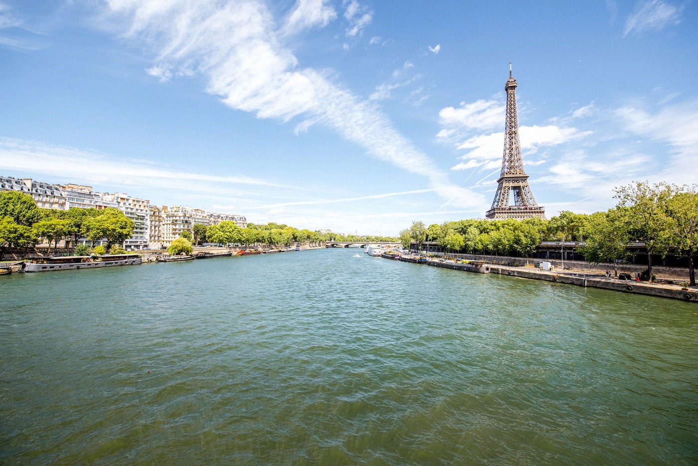 Wide-angle shot of the Seine in Paris with the Eiffel Tower in the right background, green trees along the